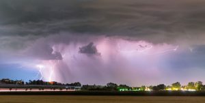 Bright lightning forks through dark storm clouds over a landscape at night.