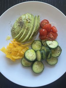 A bowl of fresh vegetables sits beside a small dish of golden olive oil.